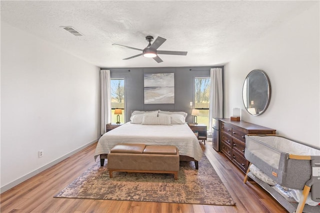 bedroom with visible vents, baseboards, wood finished floors, a textured ceiling, and a ceiling fan