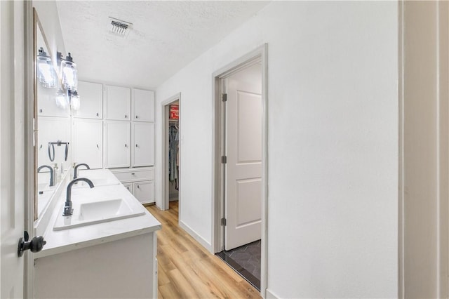 bathroom with wood finished floors, visible vents, double vanity, a sink, and a textured ceiling