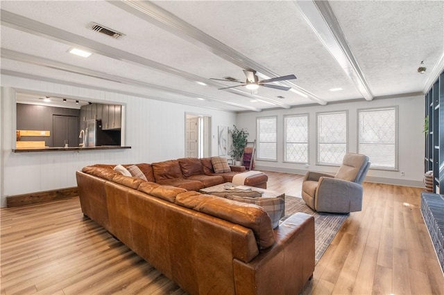living room featuring baseboards, visible vents, light wood-style floors, a textured ceiling, and beamed ceiling