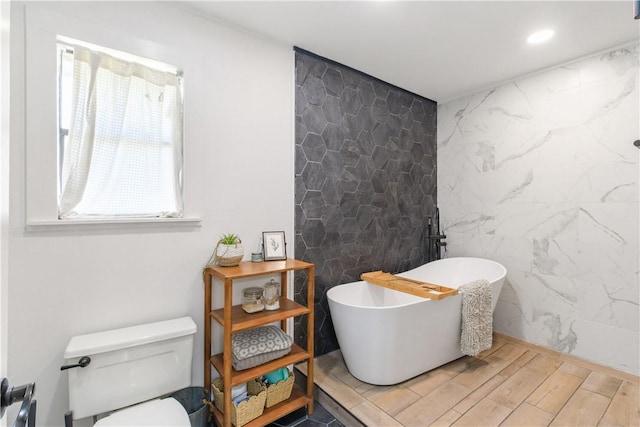 full bath featuring a soaking tub, toilet, wood finished floors, and tile walls
