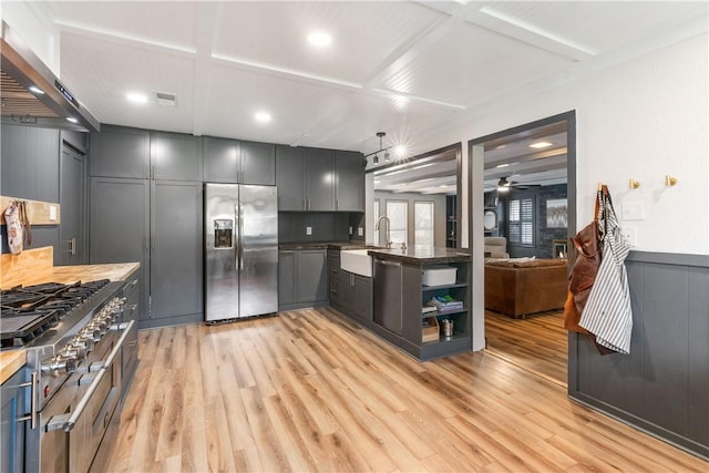 kitchen featuring light wood finished floors, wall chimney exhaust hood, appliances with stainless steel finishes, and a sink