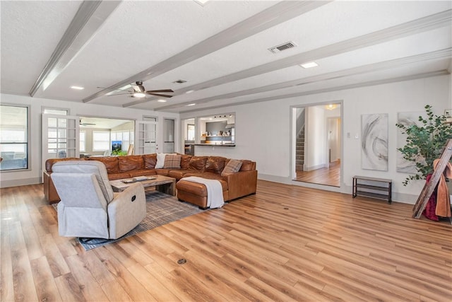 living room featuring stairway, baseboards, visible vents, beamed ceiling, and light wood-type flooring