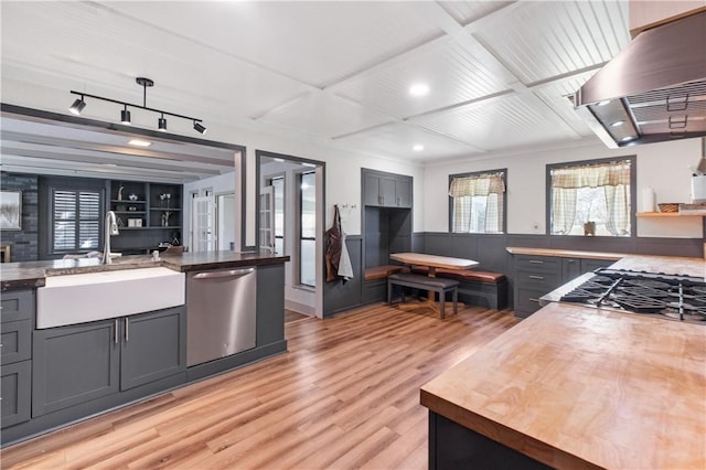 kitchen featuring butcher block countertops, a sink, wall chimney exhaust hood, light wood finished floors, and dishwasher
