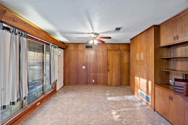 unfurnished room with wooden walls, ceiling fan, and a textured ceiling