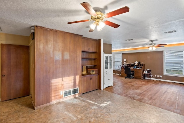 unfurnished living room featuring ceiling fan, wood-type flooring, a textured ceiling, and wooden walls