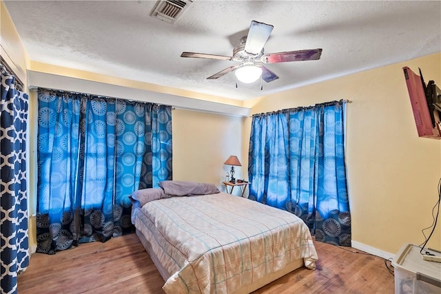 bedroom with ceiling fan, wood-type flooring, and a textured ceiling