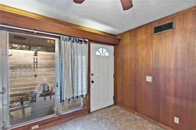 entrance foyer with wooden walls, ceiling fan, and a textured ceiling