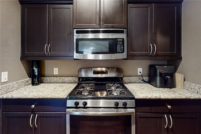 kitchen with light stone countertops, dark brown cabinets, and appliances with stainless steel finishes