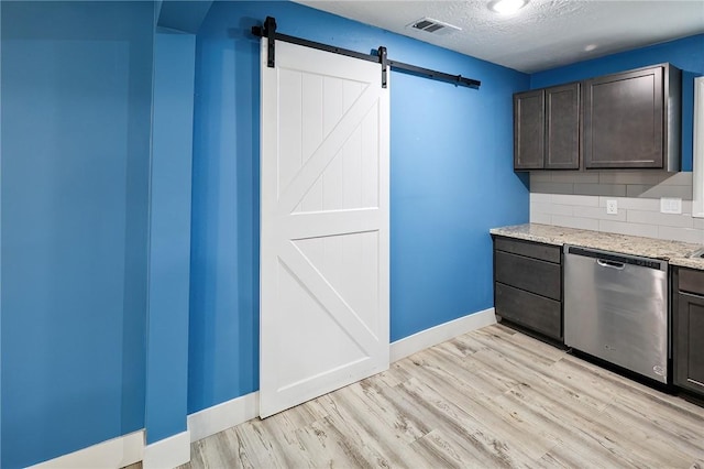 kitchen featuring light stone counters, dark brown cabinets, stainless steel dishwasher, and a barn door