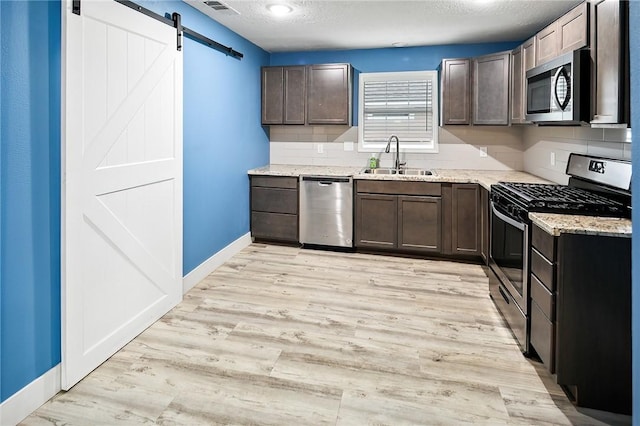 kitchen featuring sink, a barn door, stainless steel appliances, light stone countertops, and light hardwood / wood-style flooring