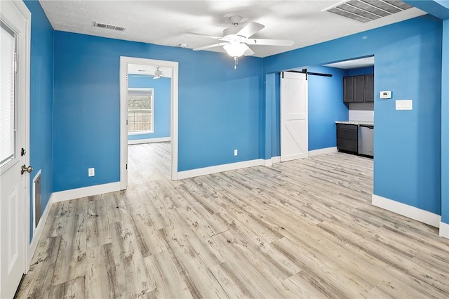 unfurnished living room with ceiling fan, a barn door, and light wood-type flooring