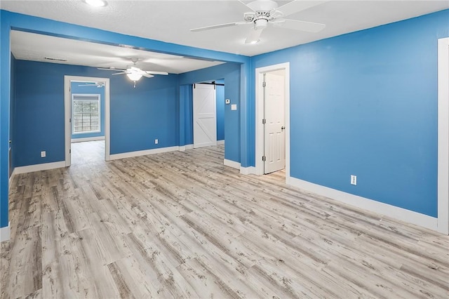 unfurnished room with ceiling fan, a barn door, and light hardwood / wood-style floors