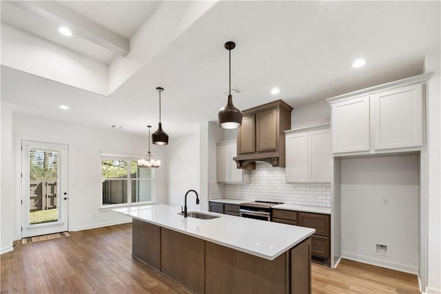 kitchen with stainless steel range oven, hanging light fixtures, a center island with sink, and sink