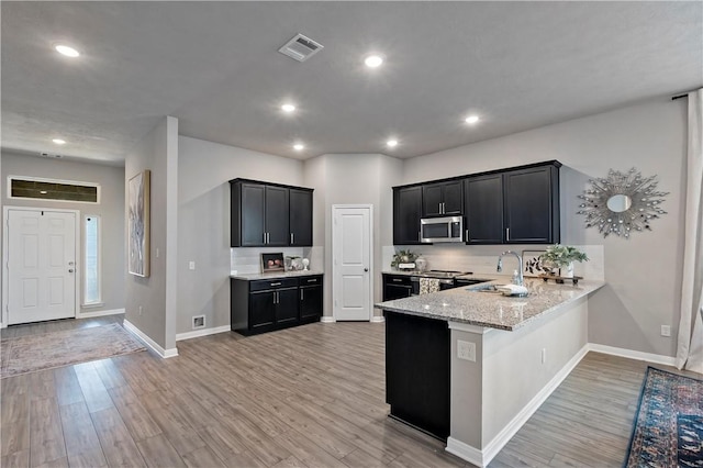 kitchen with kitchen peninsula, light stone countertops, stainless steel appliances, sink, and light hardwood / wood-style floors