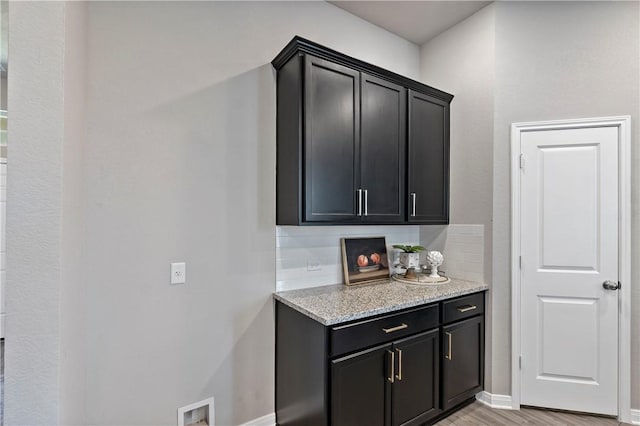 kitchen with decorative backsplash, light wood-type flooring, and light stone counters