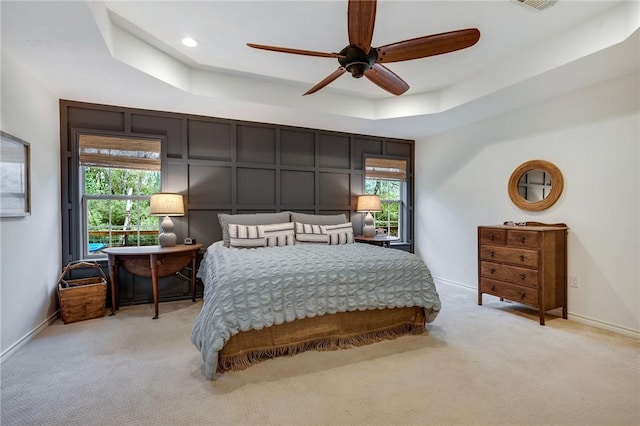 bedroom featuring light colored carpet, baseboards, a tray ceiling, and multiple windows