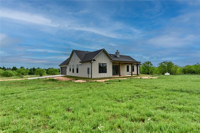 rear view of property with a chimney, board and batten siding, an attached garage, driveway, and a lawn
