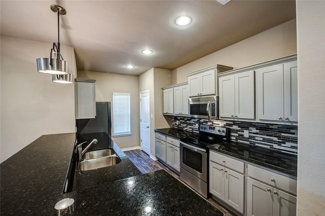 kitchen featuring pendant lighting, stainless steel appliances, backsplash, a sink, and dark stone countertops