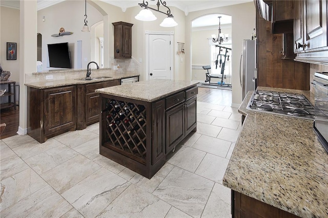 kitchen featuring dark brown cabinetry, arched walkways, decorative backsplash, ornamental molding, and a sink