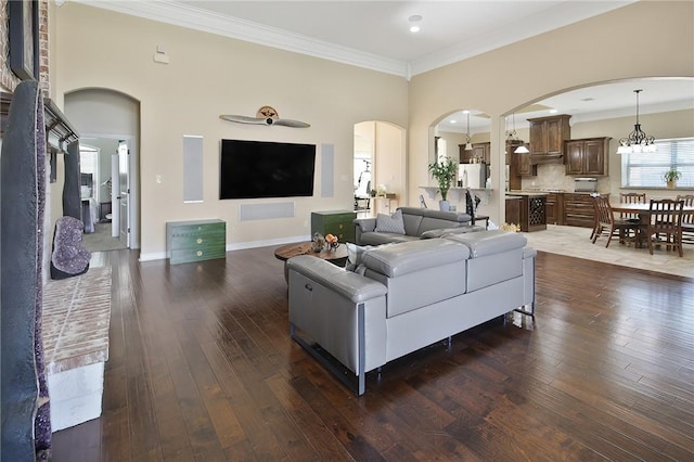 living area featuring arched walkways, ornamental molding, dark wood-style flooring, and baseboards