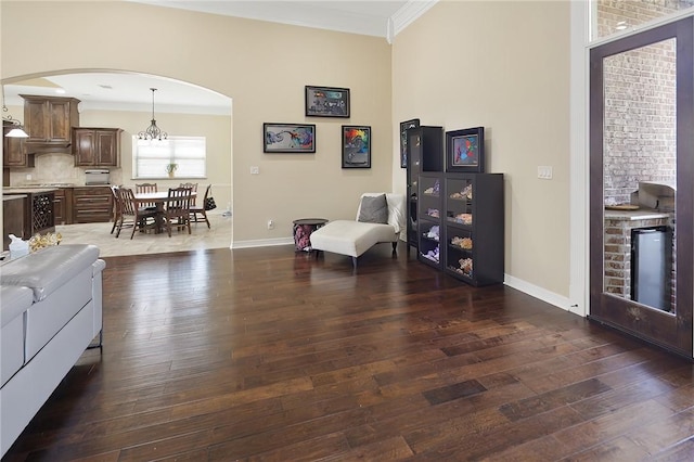 sitting room featuring baseboards, arched walkways, hardwood / wood-style floors, an inviting chandelier, and crown molding