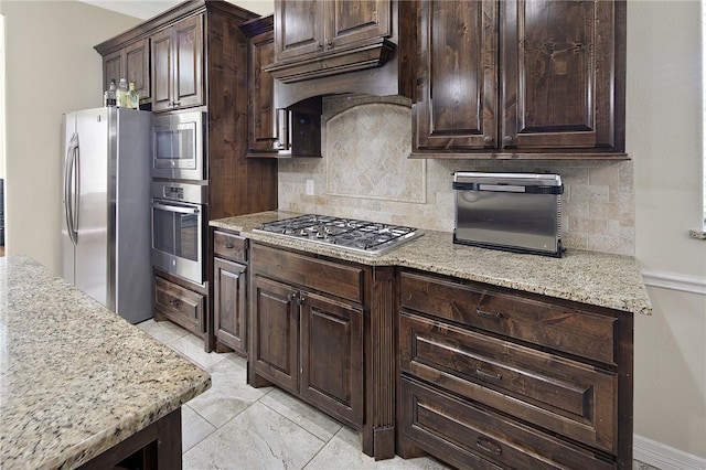 kitchen featuring custom exhaust hood, stainless steel appliances, backsplash, dark brown cabinets, and light stone countertops