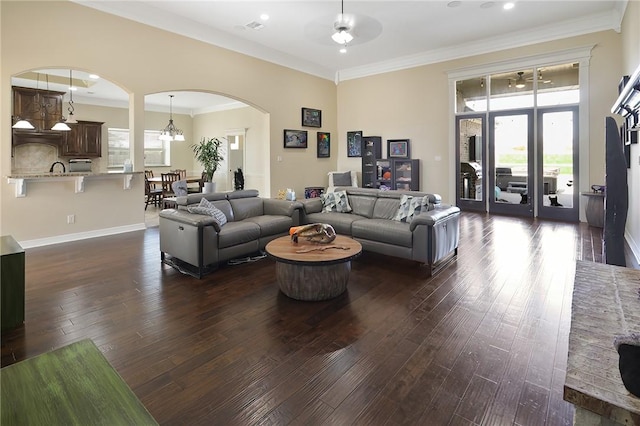 living area featuring baseboards, arched walkways, a ceiling fan, dark wood-style floors, and crown molding