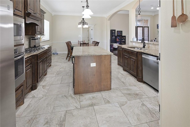 kitchen with a kitchen island, appliances with stainless steel finishes, light stone counters, and a sink