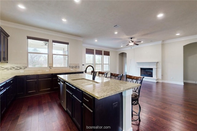 kitchen with visible vents, a fireplace with raised hearth, a sink, a kitchen bar, and dark wood-style flooring