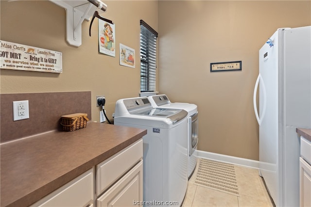 laundry area featuring washing machine and clothes dryer, light tile patterned floors, and cabinets