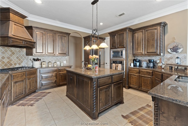 kitchen with stainless steel appliances, an island with sink, pendant lighting, dark brown cabinets, and custom range hood