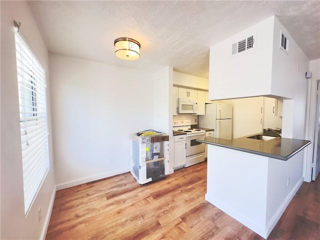 kitchen with kitchen peninsula, a textured ceiling, white appliances, sink, and light hardwood / wood-style floors