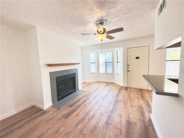 unfurnished living room with a fireplace, wood-type flooring, a textured ceiling, and ceiling fan