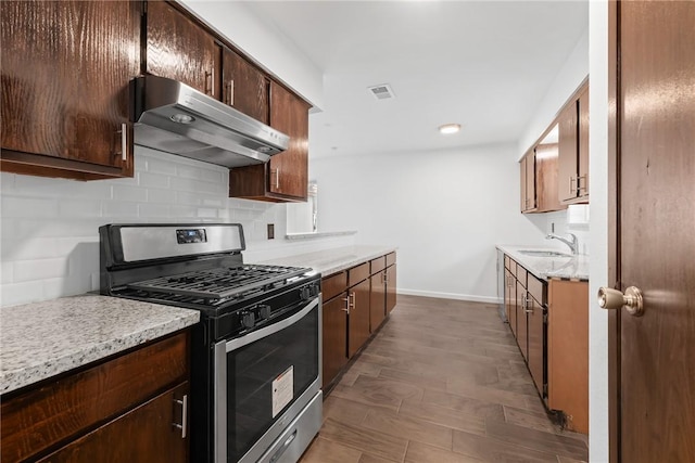 kitchen featuring decorative backsplash, light stone counters, gas stove, exhaust hood, and hardwood / wood-style floors