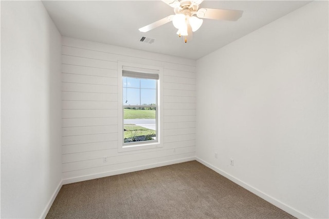 carpeted empty room with ceiling fan and wooden walls