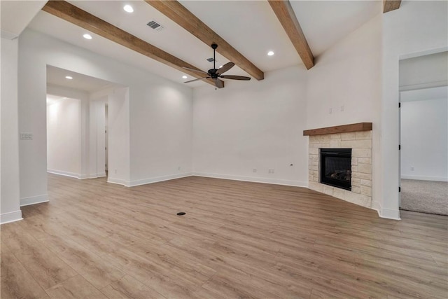 unfurnished living room with a stone fireplace, ceiling fan, beamed ceiling, and light wood-type flooring