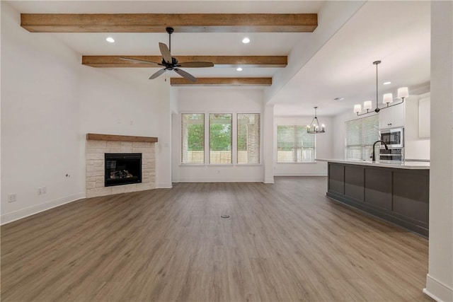 unfurnished living room featuring ceiling fan with notable chandelier, light hardwood / wood-style floors, sink, and beam ceiling