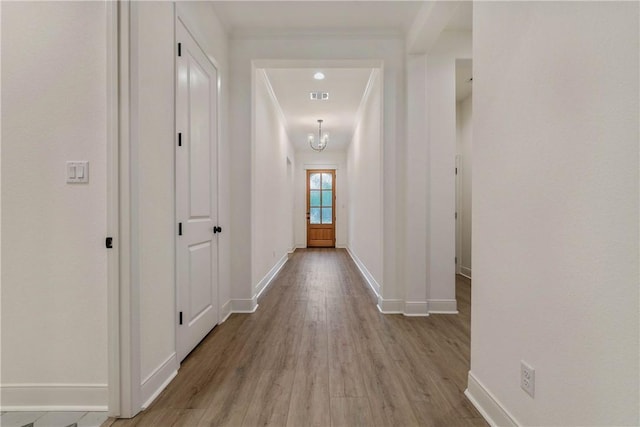 hall featuring light wood-type flooring, an inviting chandelier, and crown molding