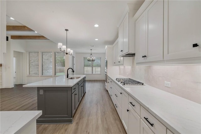 kitchen featuring white cabinetry, hanging light fixtures, light hardwood / wood-style flooring, beamed ceiling, and a center island with sink