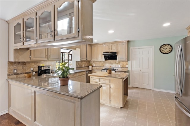 kitchen with kitchen peninsula, light stone countertops, light brown cabinets, and stainless steel appliances