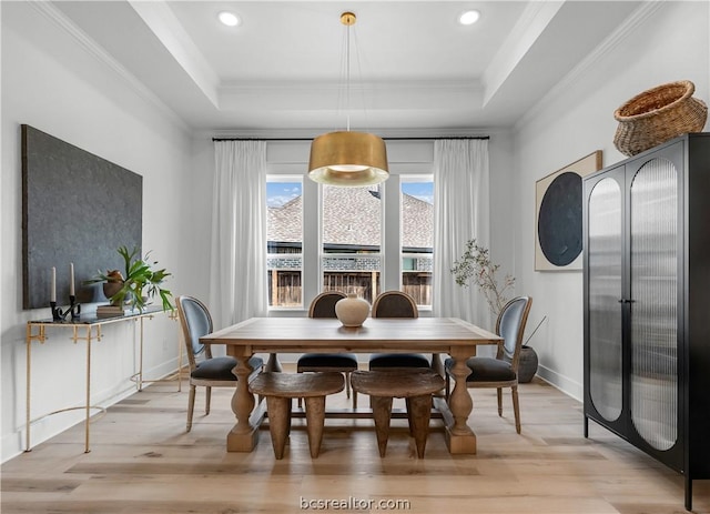 dining area with light hardwood / wood-style floors, ornamental molding, and a tray ceiling