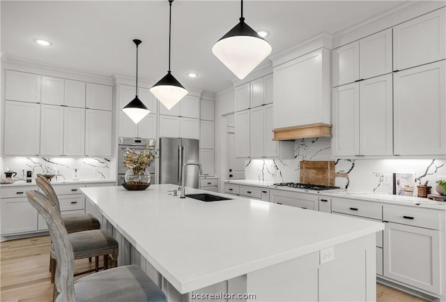 kitchen featuring appliances with stainless steel finishes, a kitchen island with sink, sink, pendant lighting, and white cabinets