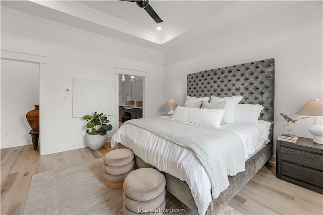 bedroom with ensuite bathroom, ceiling fan, ornamental molding, a tray ceiling, and light hardwood / wood-style floors