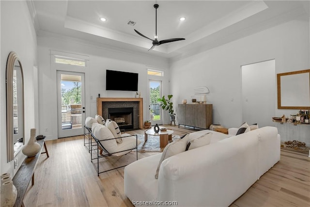 living room with a raised ceiling, crown molding, ceiling fan, and light wood-type flooring