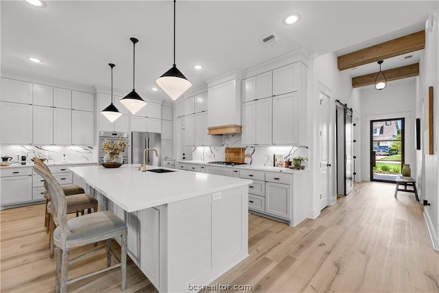 kitchen featuring white cabinetry, a kitchen island with sink, beamed ceiling, and light wood-type flooring