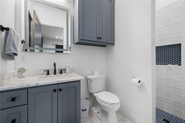 bathroom with tiled shower, vanity, baseboards, and toilet