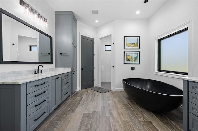 bathroom with a soaking tub, wood finished floors, vanity, and visible vents