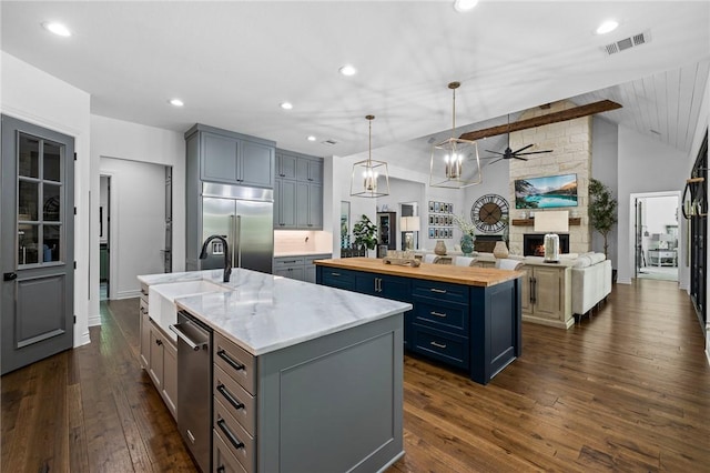 kitchen featuring visible vents, open floor plan, wooden counters, appliances with stainless steel finishes, and an island with sink