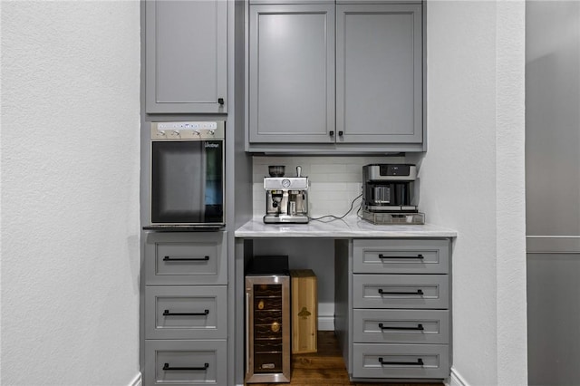 bar with tasteful backsplash, beverage cooler, baseboards, and stainless steel oven