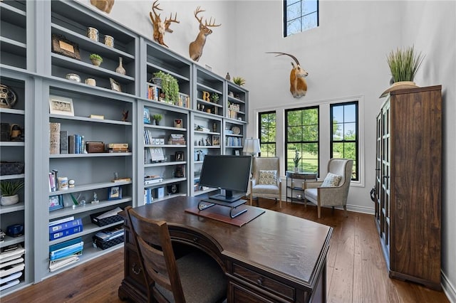 office area featuring a towering ceiling and dark wood-style floors